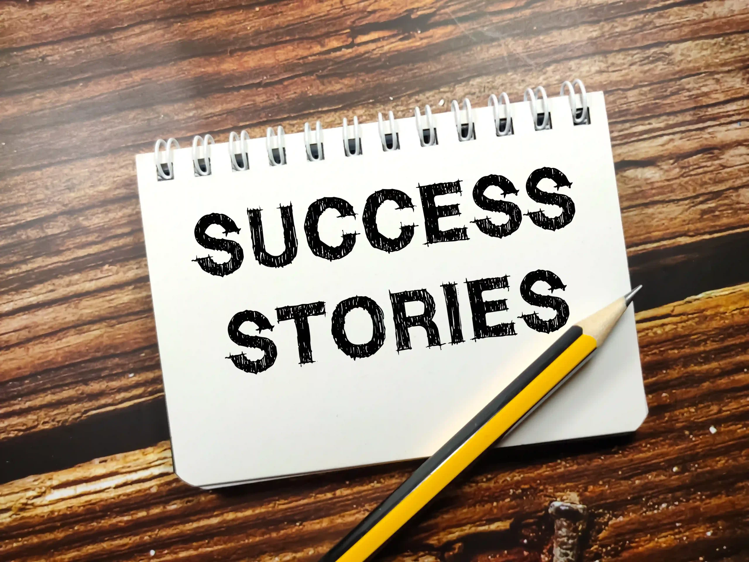business-concepttext-success-stories-notebook-with-pencil-wooden-background business-concepttext-success-stories-notebook-with-pencil-wooden-background