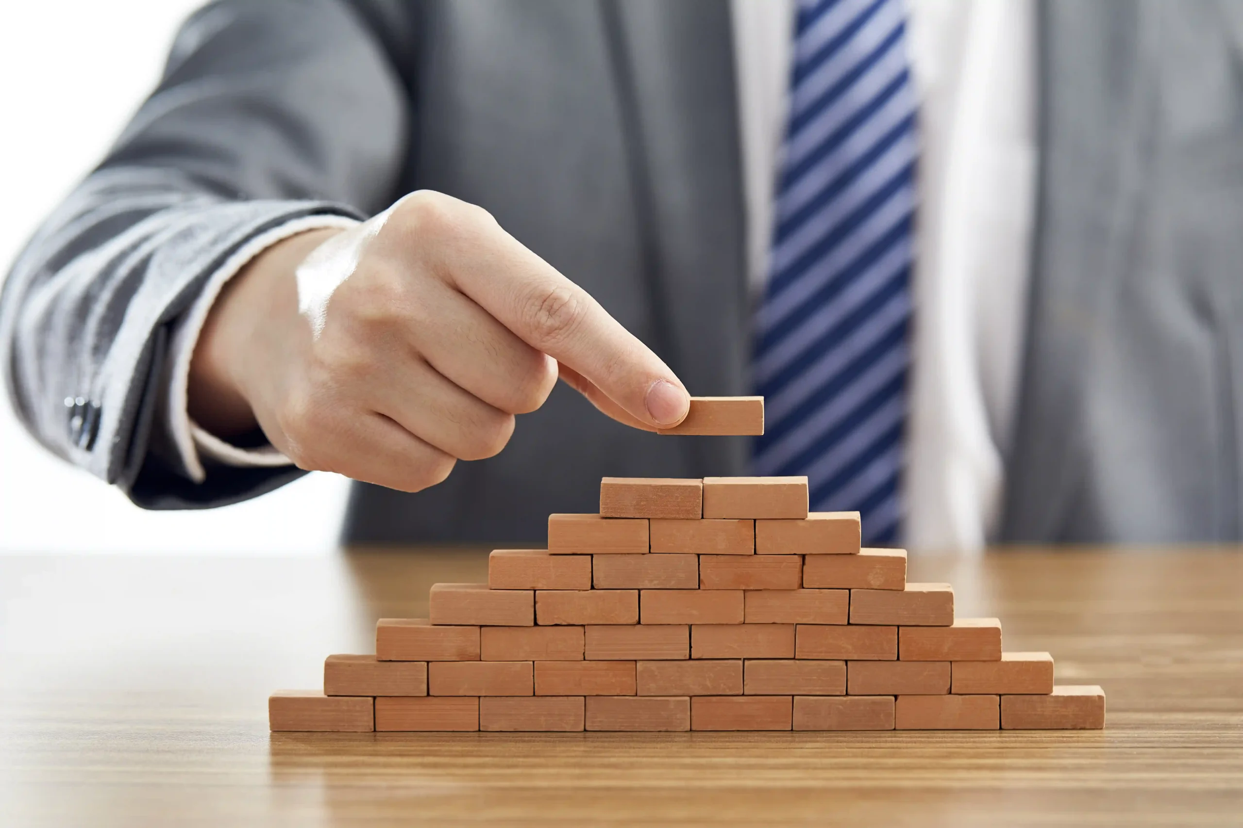businessman-suit-putting-last-piece-pyramid-using-wooden-blocks businessman-suit-putting-last-piece-pyramid-using-wooden-blocks
